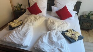 Un letto rifatto con lenzuola bianche, due cuscini rossi e una coppia di asciugamani piegati.