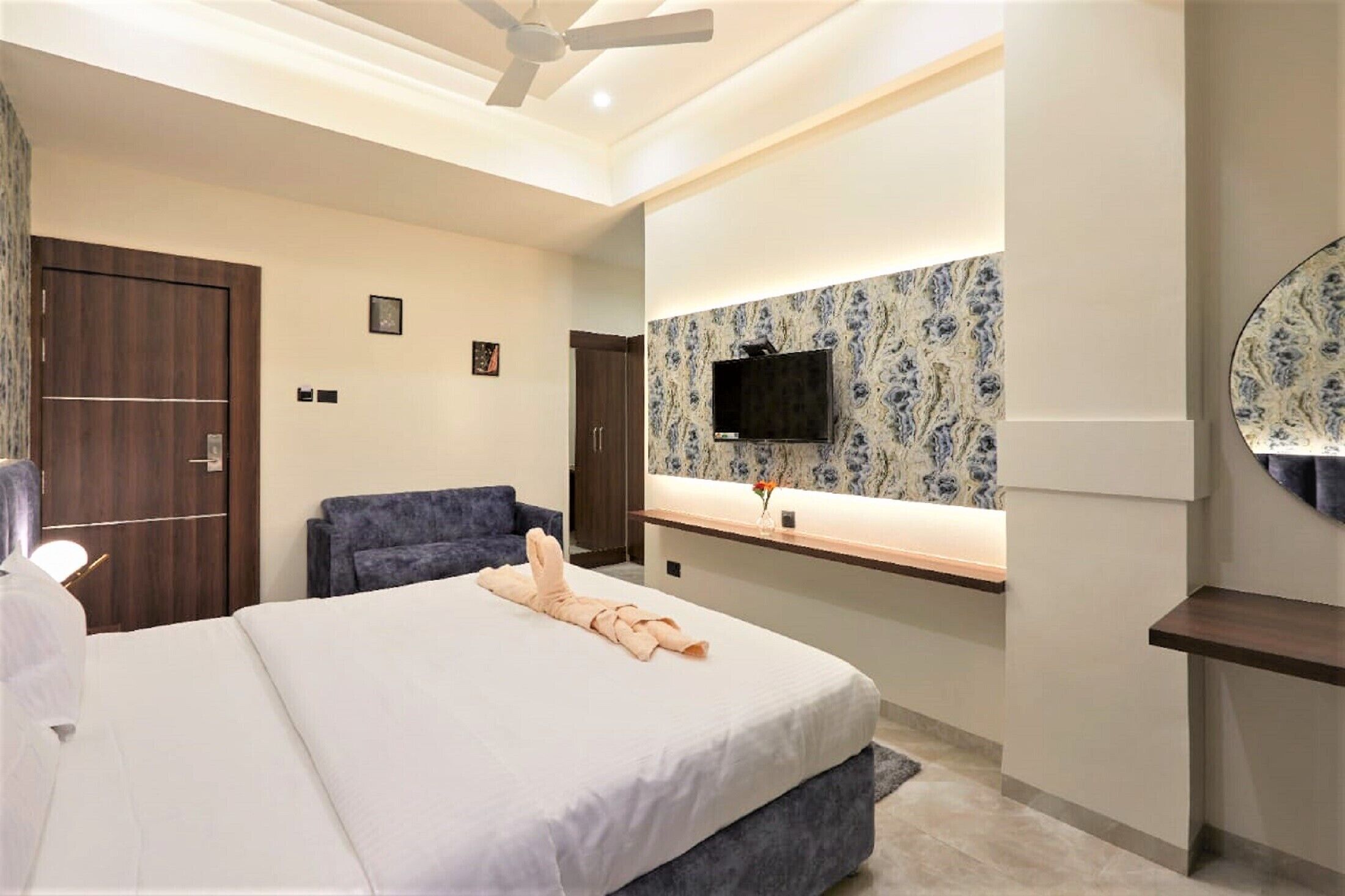 Une chambre d’hôtel moderne dotée d’un grand lit, d’un téléviseur à écran plat fixé au mur, d’un ventilateur de plafond et d’une armoire en bois.