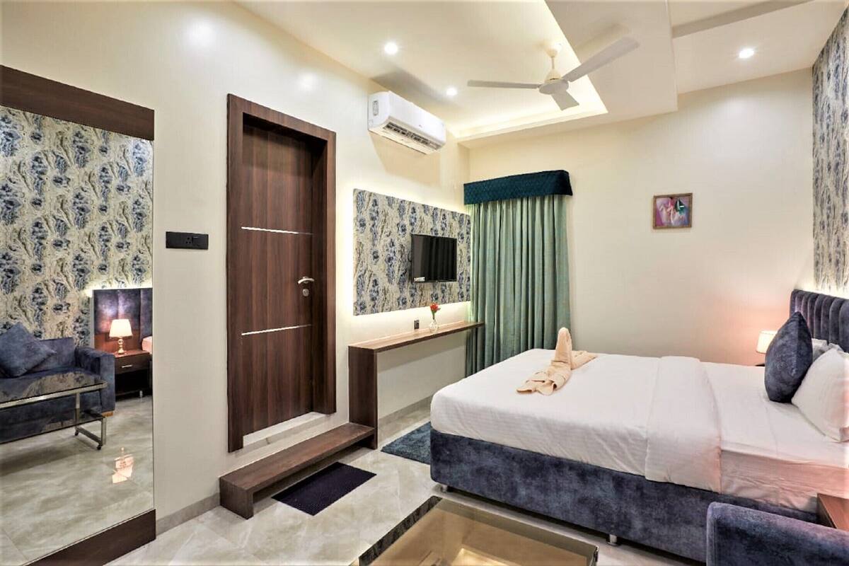 Habitación de hotel con cama, escritorio, televisión, armario y ventilador de techo.