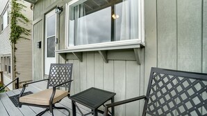 A covered outdoor seating area with two chairs and a small table, adjacent to a building with a window and a light fixture. - Modern Rustic Charm with City Views (Cincinnati)