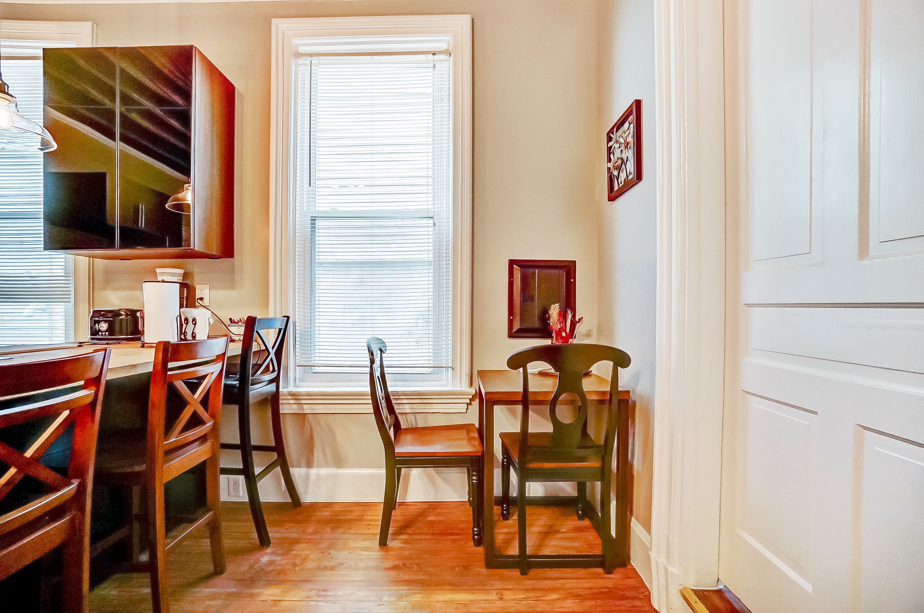 A dining area with wooden chairs and a table, a window with blinds, and a wall-mounted cabinet.