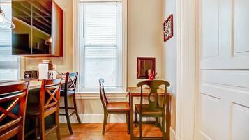 A dining area with wooden chairs and a table, a window with blinds, and a wall-mounted cabinet.