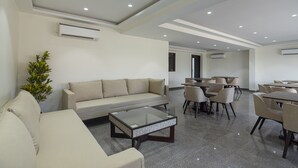 A modern hotel lobby with a beige sofa, a glass coffee table, and a dining area with tables and chairs. - Deluxe Double Room with Balcony (Jaipur)