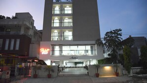 A multi-story hotel with a neon sign, a gated entrance, and potted plants. - Deluxe Double Room with Balcony (Jaipur)