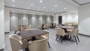 A modern conference room with multiple tables and chairs, a large window with curtains, and a sofa area. - Deluxe Double Room with Balcony (Jaipur)