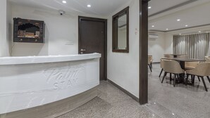 A hotel reception area with a reception desk, a mirror, a door, and a dining area with tables and chairs. - Deluxe Double Room with Balcony (Jaipur)