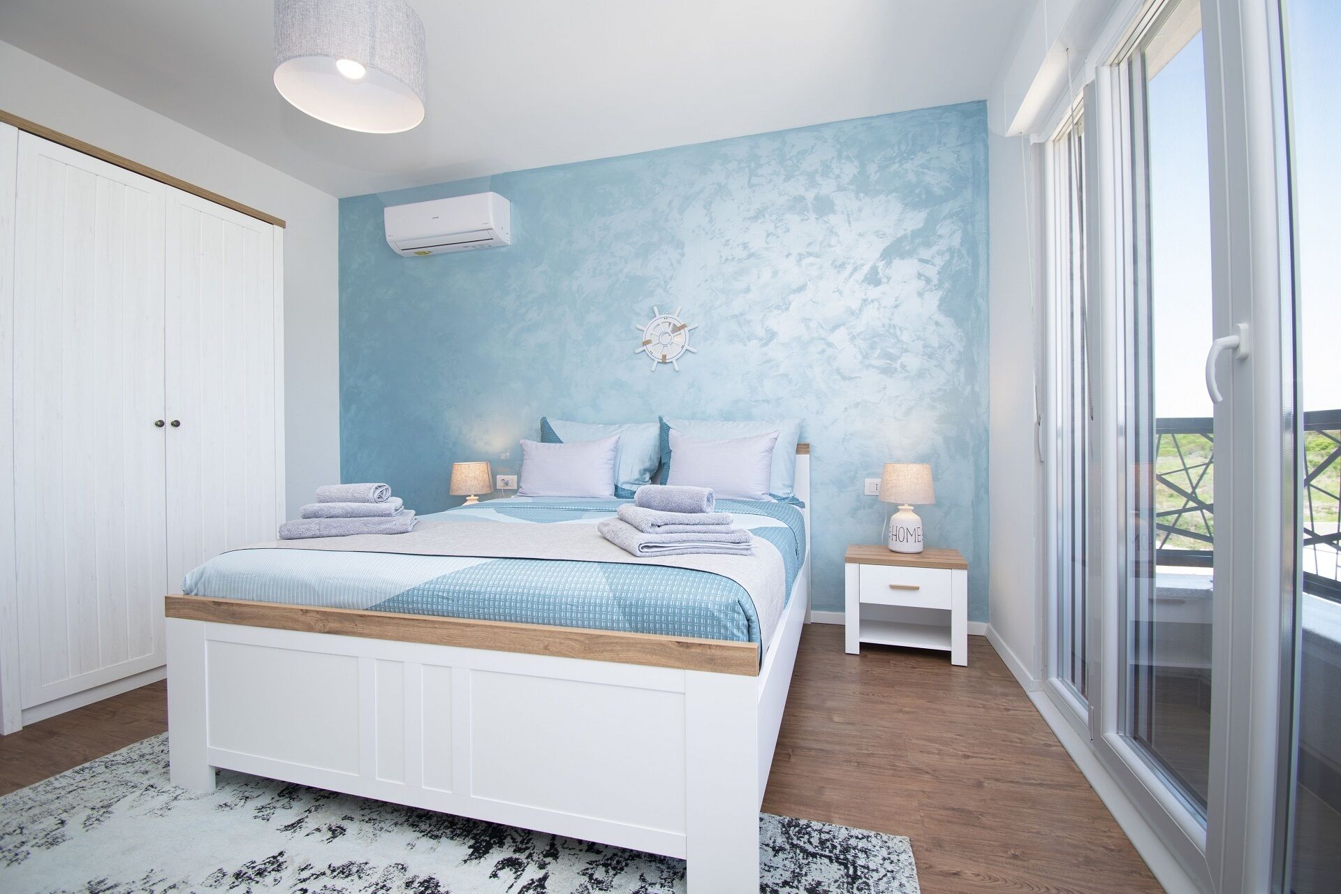 A bedroom with a bed, bedside tables, a wardrobe, and a view through a glass door.