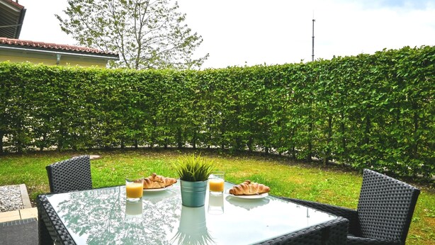 Una mesa de vidrio con cruasanes, un vaso de jugo de naranja y una planta en una maceta de metal.