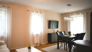 Una sala de estar moderna con comedor, un televisor de pantalla plana montado en la pared y una araña.