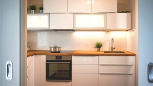 Una cocina compacta con armarios blancos, una encimera de madera, un horno de acero inoxidable y un lavamanos.