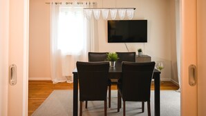 Un comedor con una mesa, sillas, un televisor de pantalla plana y un ventanal con cortinas.