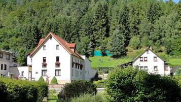 Ein weißes Gebäude mit rotem Dach, umgeben von üppiger Vegetation und einem bewaldeten Hang.
