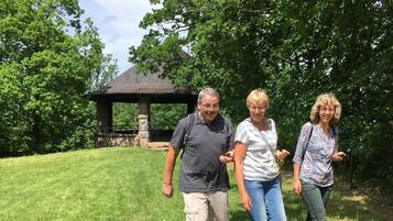 Trois personnes se promènent sur une pelouse, avec un kiosque en arrière-plan.