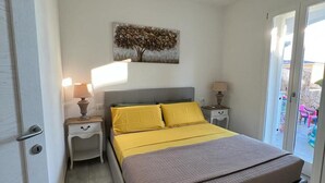 A bedroom with a bed, two bedside tables with lamps, a ceiling light, and a window with a view. - Enchanting Holiday Apartment in Lu Bagnu (Castelsardo)