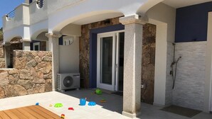 A modern house with a stone exterior, a wooden deck, and a covered outdoor area with toys. - Enchanting Holiday Apartment in Lu Bagnu (Castelsardo)