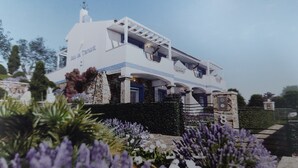 A modern two-story house with a stone facade, multiple balconies, and a garden with purple flowers. - Enchanting Holiday Apartment in Lu Bagnu (Castelsardo)