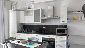 A compact kitchen with white cabinets, a black countertop, a built-in oven, and a microwave. - Enchanting Holiday Apartment in Lu Bagnu (Castelsardo)
