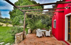 A patio with a pergola, white wicker furniture, and a red building wall.