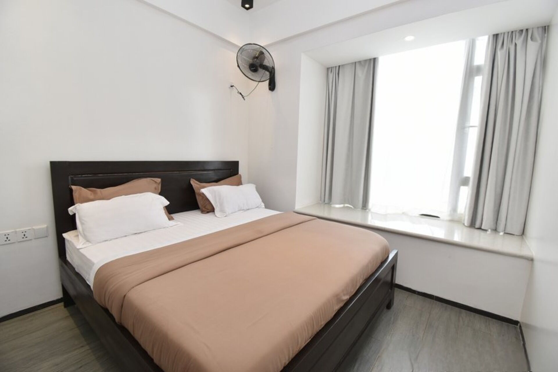 Una habitación de hotel moderna con una cama grande, un ventanal con cortinas y un ventilador de pared.