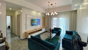 Een moderne woonkamer met een flatscreen televisie, blauwgroene banken, een glazen salontafel en een plafondlamp.