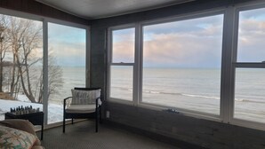 Una habitación con un amplio ventanal con vistas al océano, una silla con cojín y un tablero de ajedrez sobre una mesa.