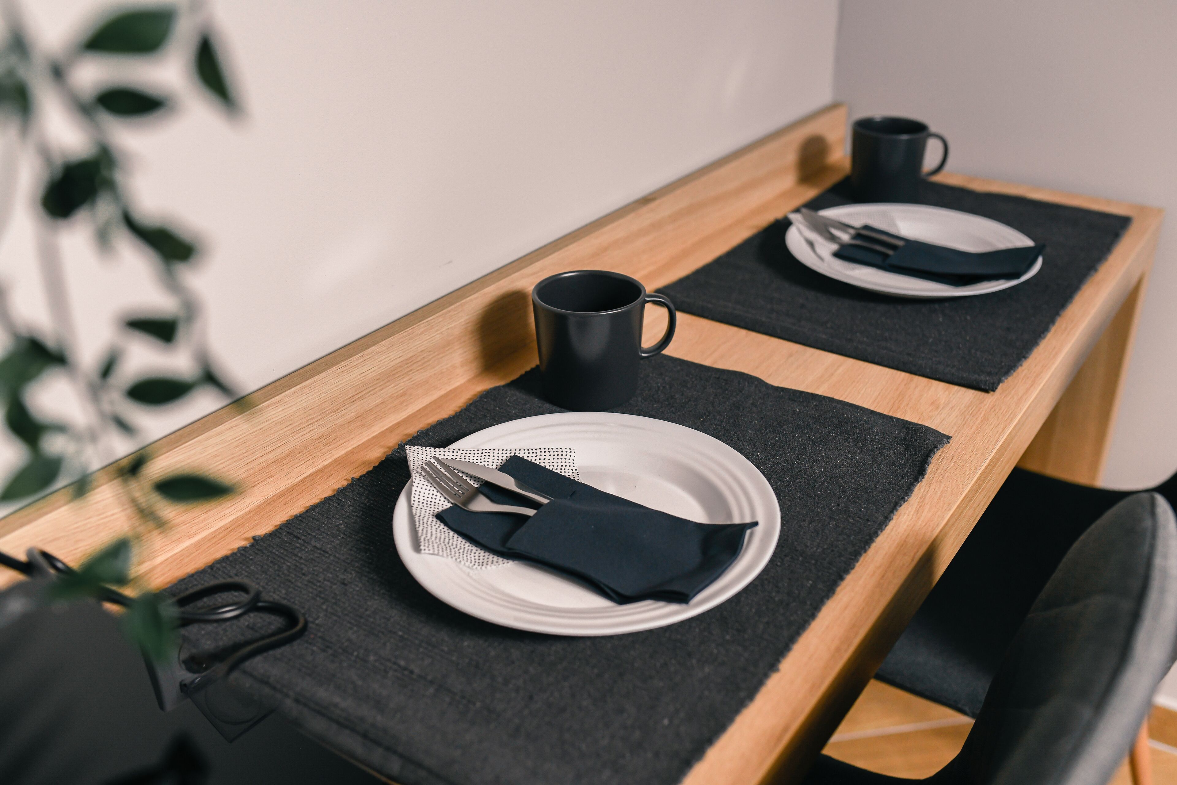 A dining table with a black placemat, a white plate, a black napkin, a fork, a knife, and a black mug.