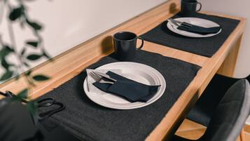 Una mesa de comedor con un mantel individual negro, un plato blanco, una servilleta negra, un tenedor, un cuchillo y una taza negra.