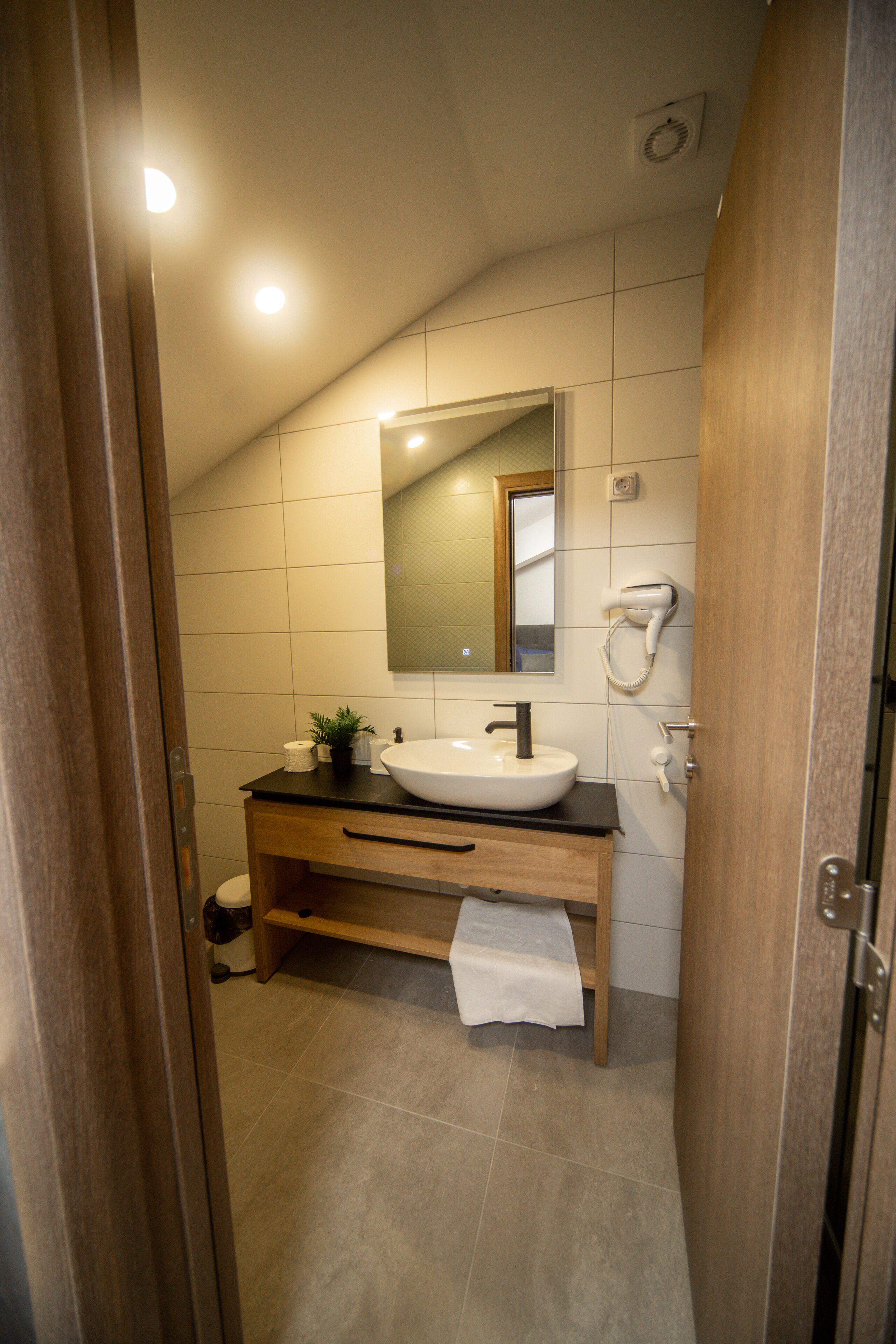 A modern bathroom with a white sink, wooden vanity, and a towel rack.