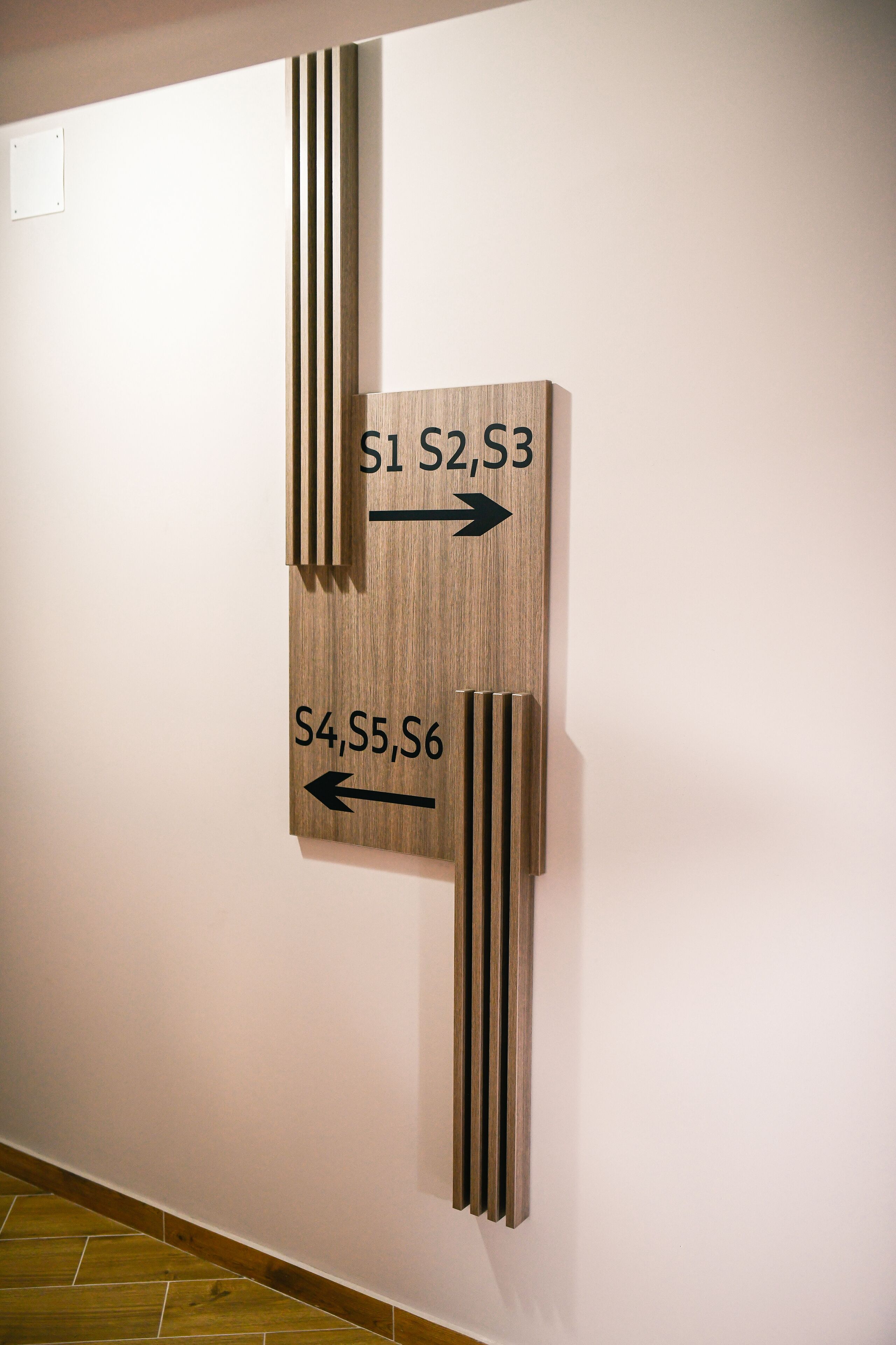 A directional sign with arrows pointing to different room numbers.