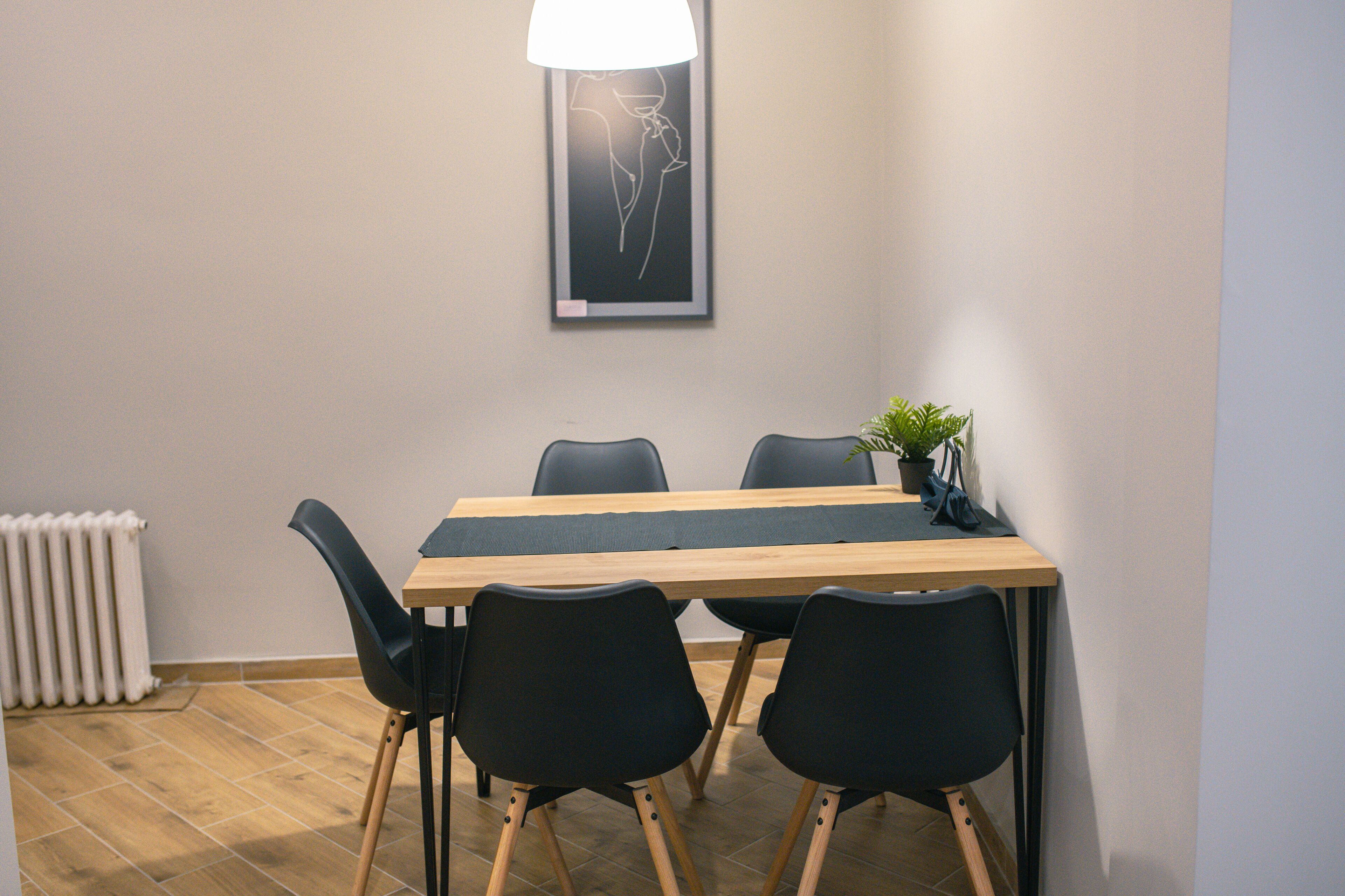 Un salón de conferencias con una mesa de madera, cuatro sillas negras, una planta en maceta y una obra de arte abstracta enmarcada en la pared.