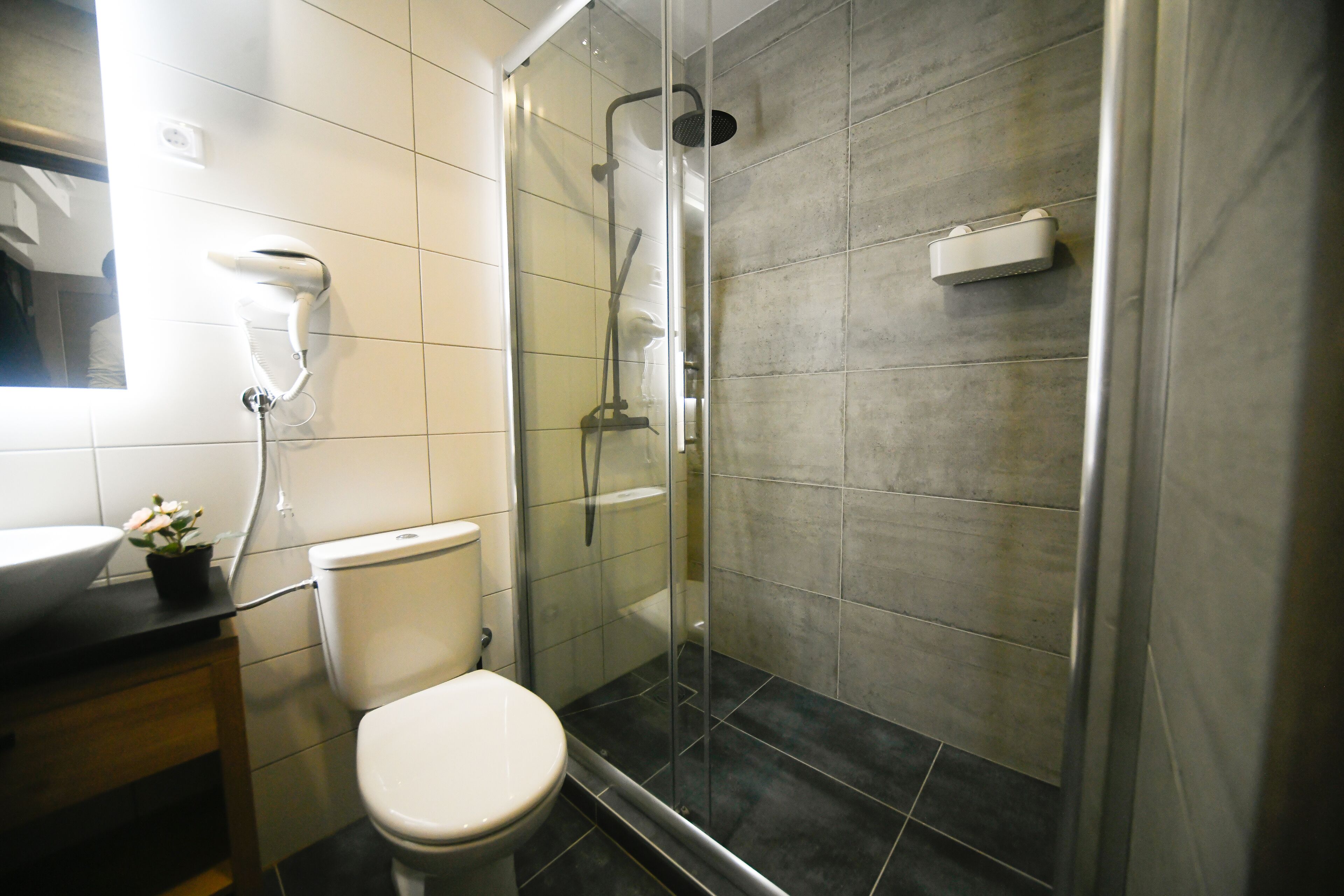 Un baño moderno con ducha de vidrio, inodoro y lavamanos con espejo.