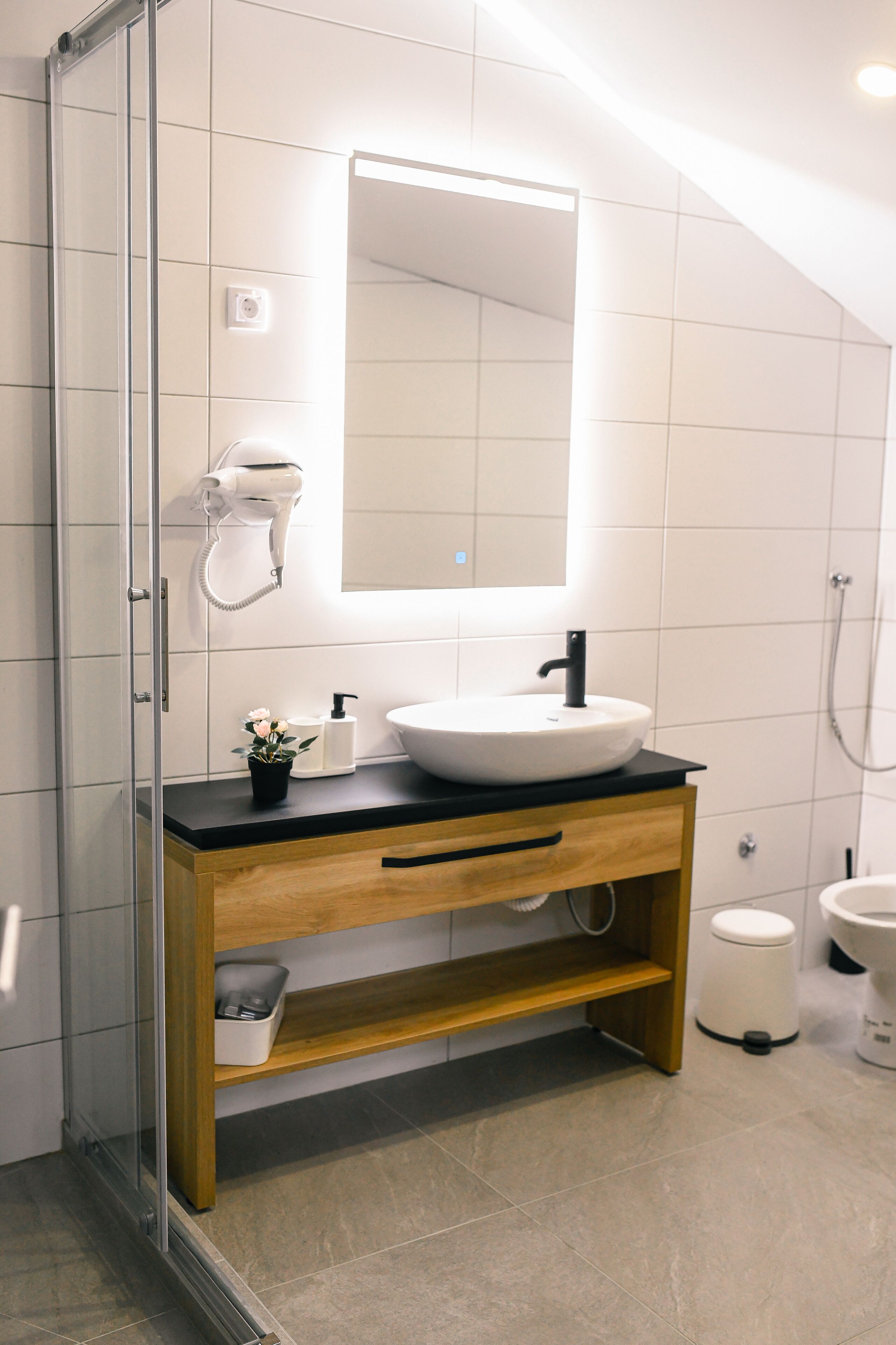 A modern bathroom with a glass shower enclosure, a white sink with a black faucet, and a wooden vanity.