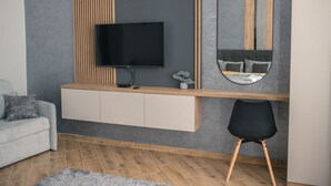 Een moderne woonkamer met een flatscreen televisie bevestigd aan een houten paneel, een inbouwkast eronder en een ronde spiegel aan de muur.