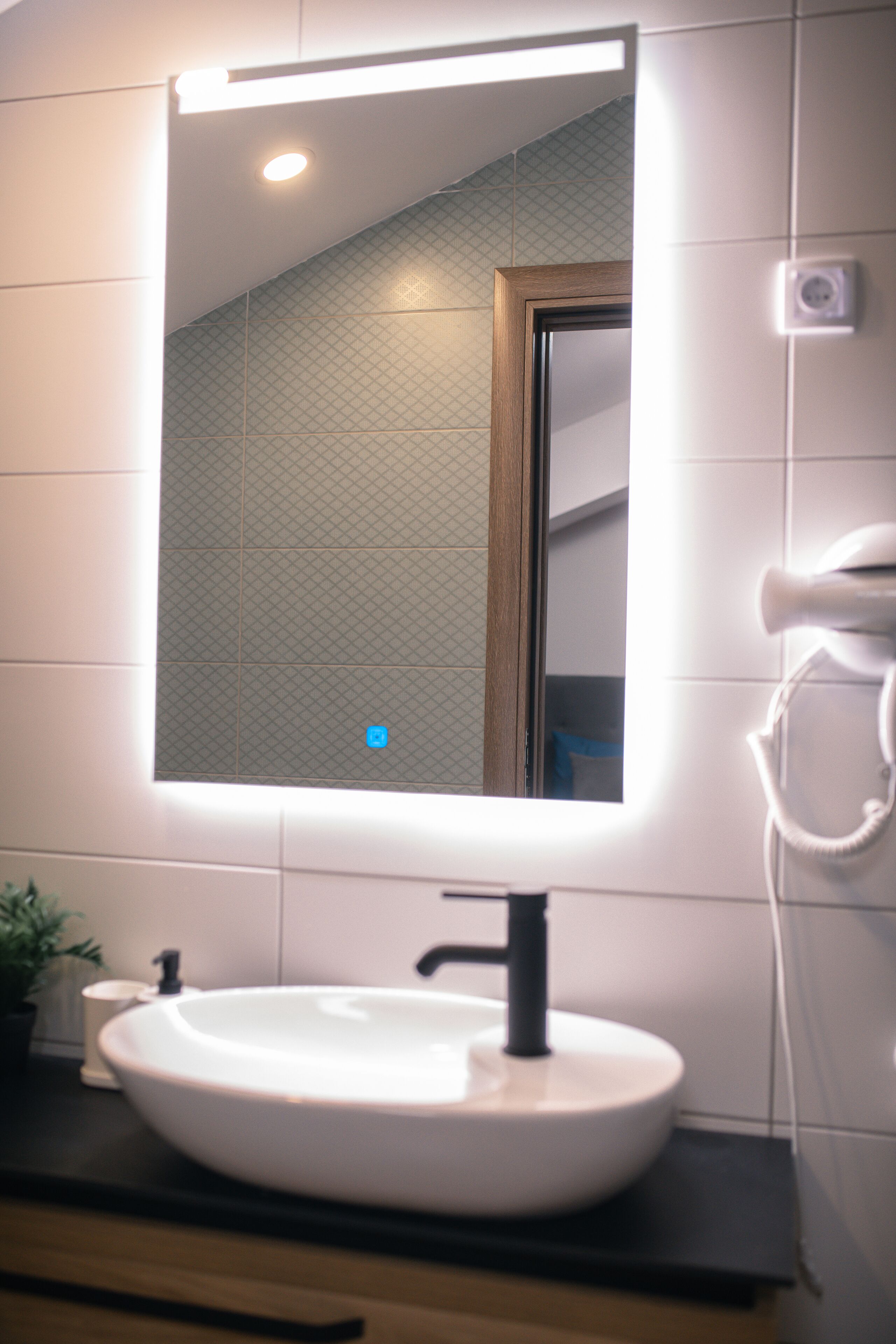 A bathroom with a white sink, a mirror, and a hairdryer on the wall.