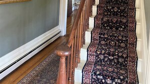 A grand staircase with ornate carpet and a wooden handrail, leading to a room with a framed historical painting and a hanging lantern. - Historic Home at Sheldrake in the Finger Lakes. (Ovid)