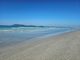 Uma praia com águas azul-claras, margem de pedrinhas e montanhas ao longe.