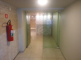 Um corredor com um extintor fixado na parede, chão em azulejo e uma porta que dá para um quarto com parede estampada.
