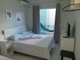 Quarto de hotel com cama, mesa de cabeceira, televisão e vista para o exterior.