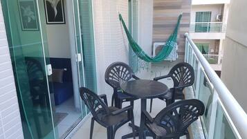 Varanda com mesa, cadeiras e rede, além de porta de vidro que dá para o interior.