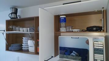 Uma cozinha com micro-ondas, prateleiras com louças e uma cafeteira.