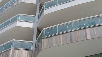 A multi-story building with a modern design, featuring balconies with glass railings and a visible logo on the lower part of the facade.