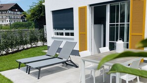 Une terrasse extérieure moderne, dotée de deux fauteuils de relaxation, d’une table et de chaises.
