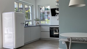 Une cuisine moderne avec des meubles blancs, un four encastré et un coin repas comprenant une table et des chaises.