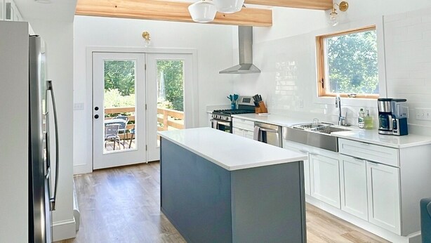 Une cuisine moderne dotée d’un îlot central, de poutres en bois et offrant une vue sur l’extérieur.