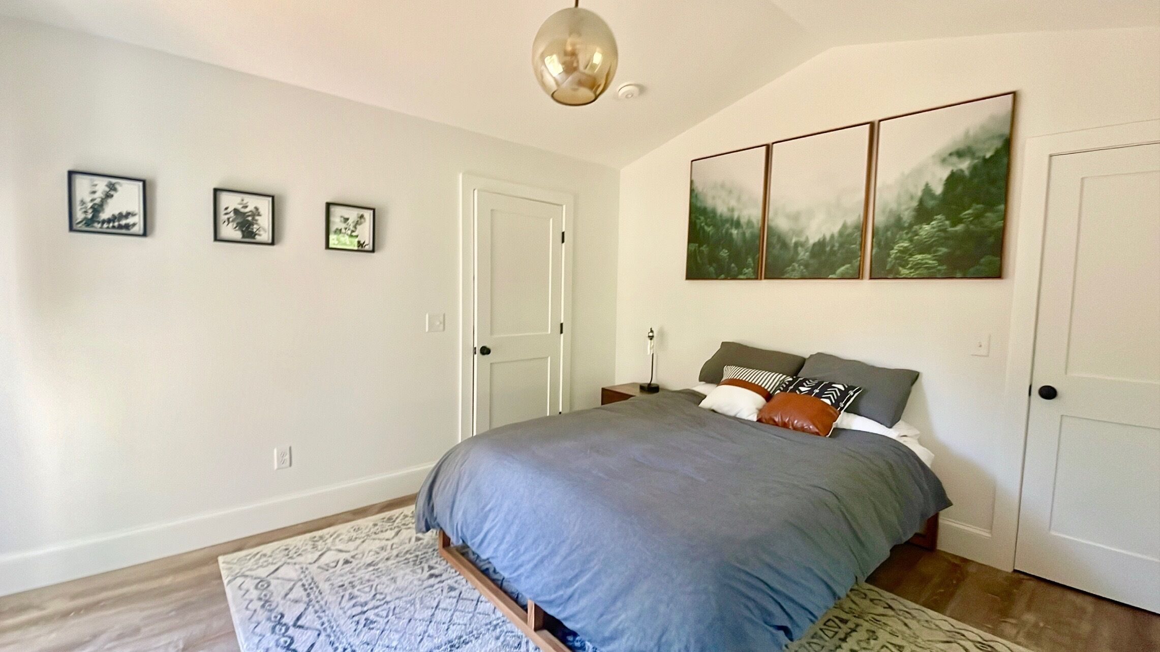 A bedroom with a bed, a rug, and three framed pictures on the wall.