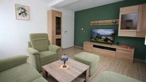 A living room with a green sofa set, a wooden TV stand with a flat-screen TV, and a small table with a decorative lamp. - 4-star vacation apartment "Sorbitztal" incl. guest card Schwarzatal (Rohrbach)