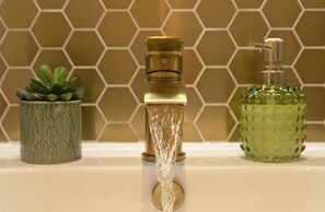 Un baño con un grifo moderno, una botella verde con textura y una planta estampada.