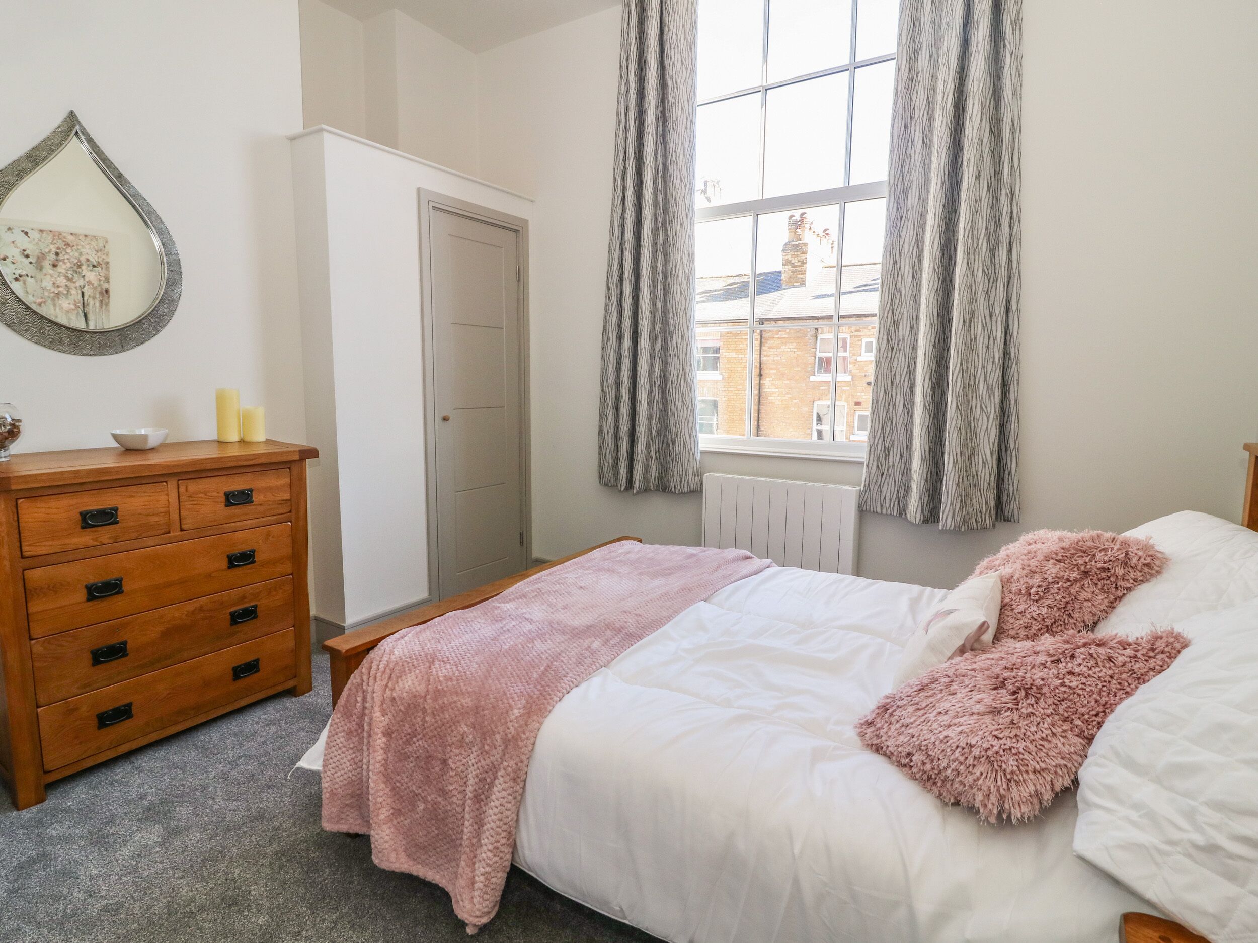 A bedroom with a bed, a dresser, a window with curtains, and a radiator.