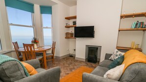 A living room with grey sofas, a wooden coffee table, a TV mounted on the wall, and a fireplace. - Apartment 6 Bay View (Scarborough)