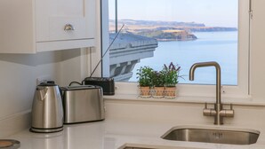 A kitchen with a stainless steel sink, a toaster, a kettle, and a radio. There are potted plants on the windowsill. - Apartment 6 Bay View (Scarborough)